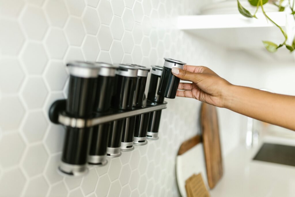 Hand placing spice container on kitchen wall-mounted magnetic rack. Modern organization.