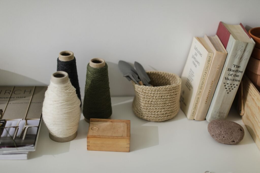 A serene home setup featuring yarn spools, books, and decor items on a white shelf for a cozy ambiance.